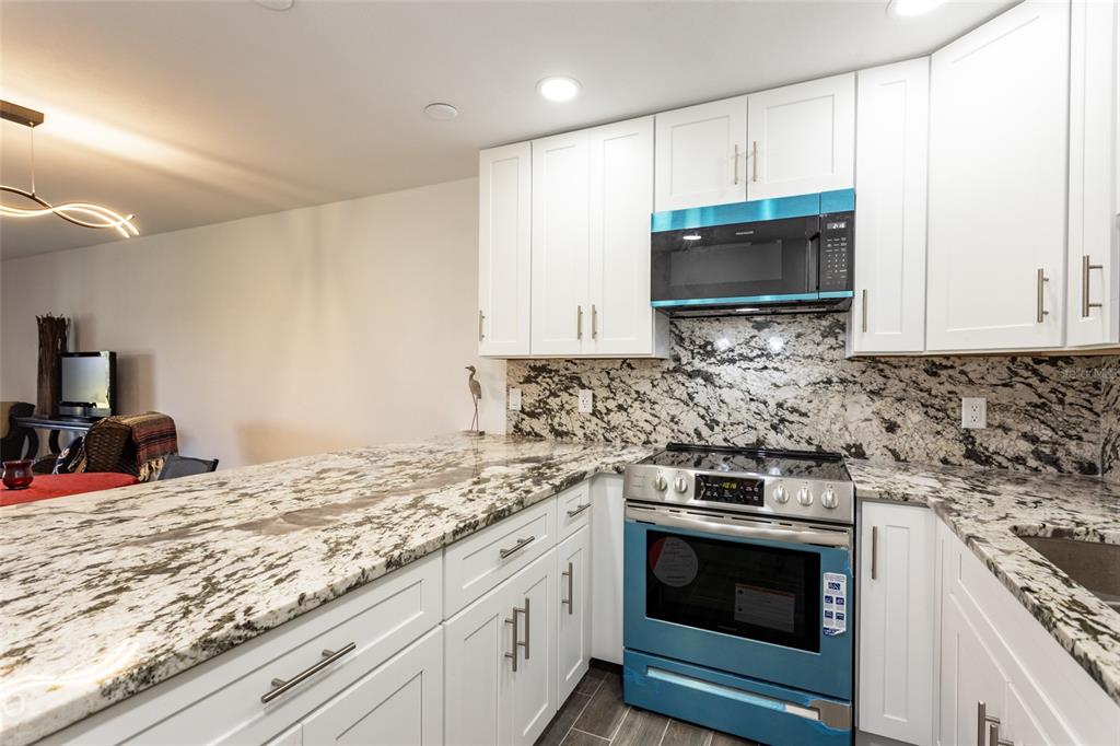 A kitchen features white cabinets, granite countertops, and a blue microwave and oven range — 23 OCEAN PALM VILLA DRIVE N, FLAGLER BEACH, FL