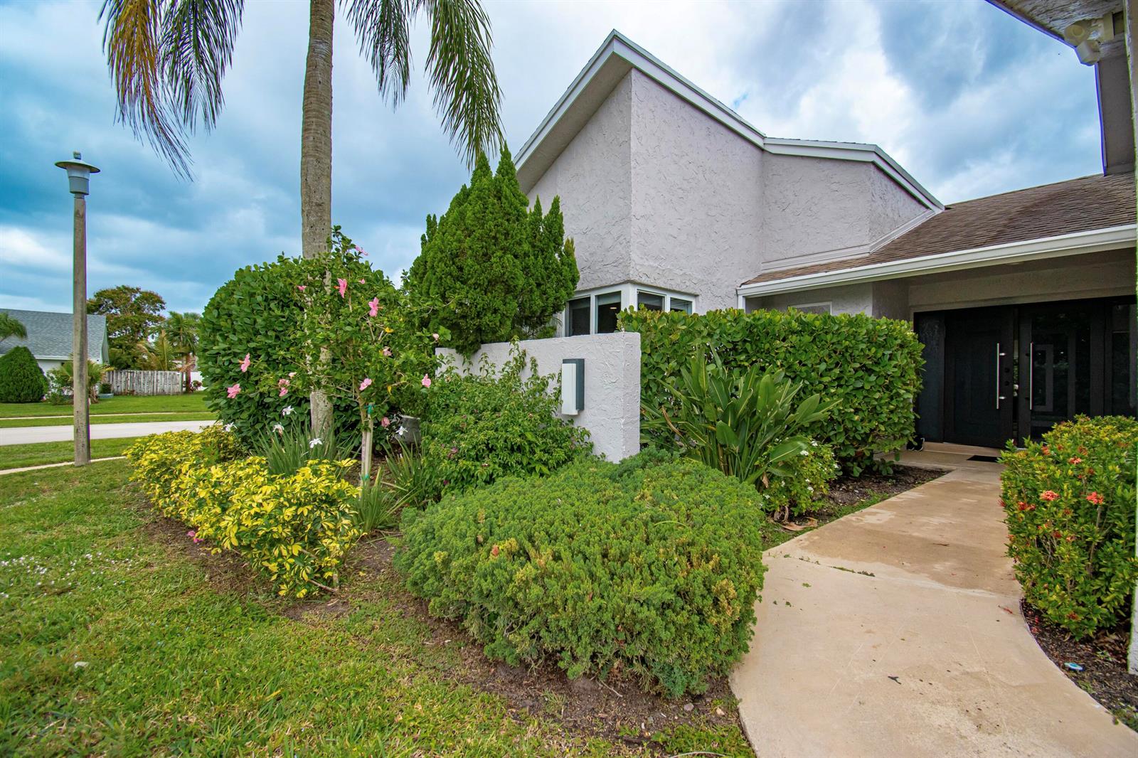 A light-colored house exterior features a concrete walkway, lush landscaping, and a palm tree — 7484 Malibu Crescent, Boca Raton FL 33433, BOCA RATON, FL
