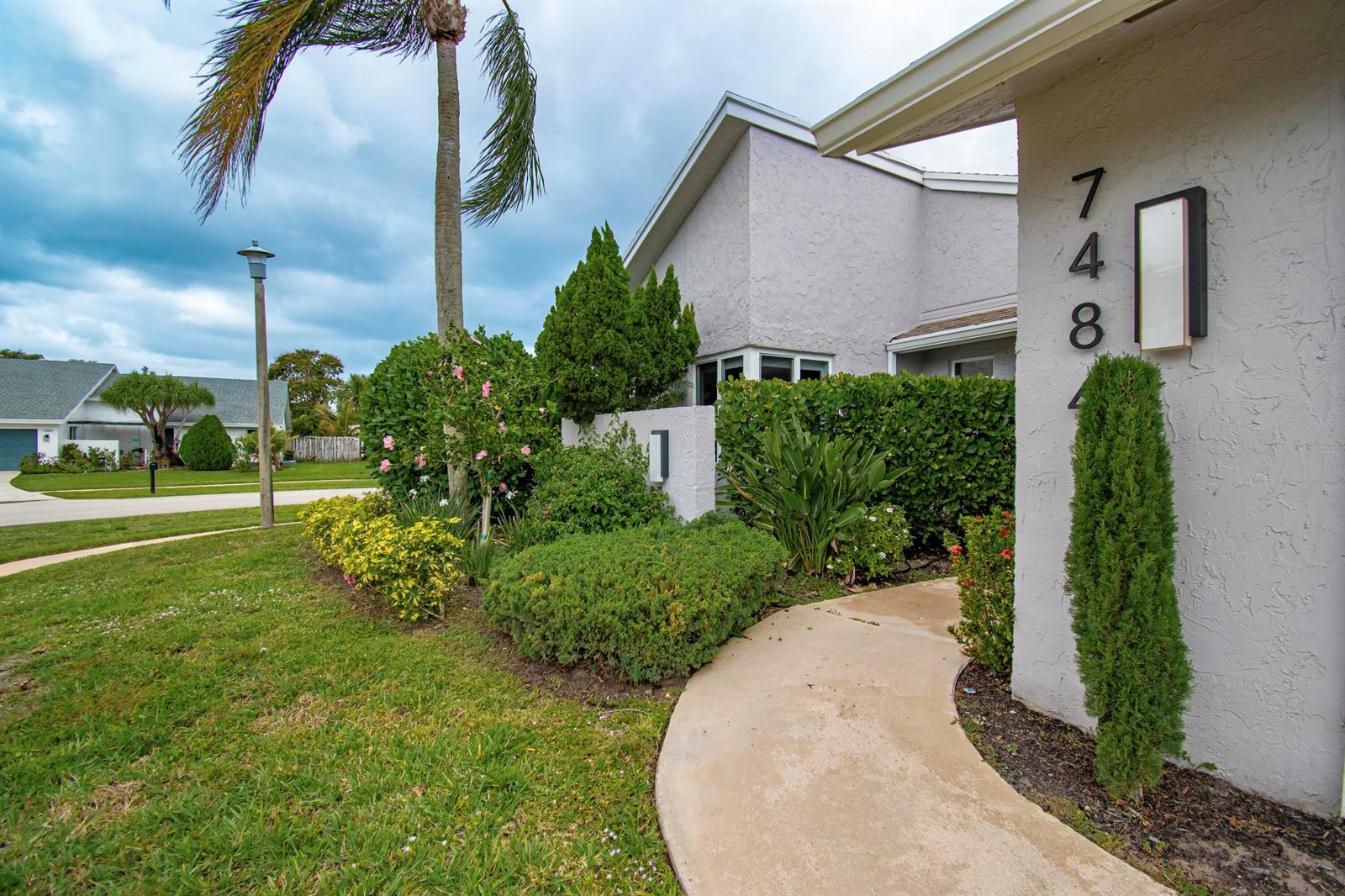 A curved concrete walkway leads to the entrance of a light-colored home with landscaping — 7484 Malibu Crescent, Boca Raton FL 33433, BOCA RATON, FL
