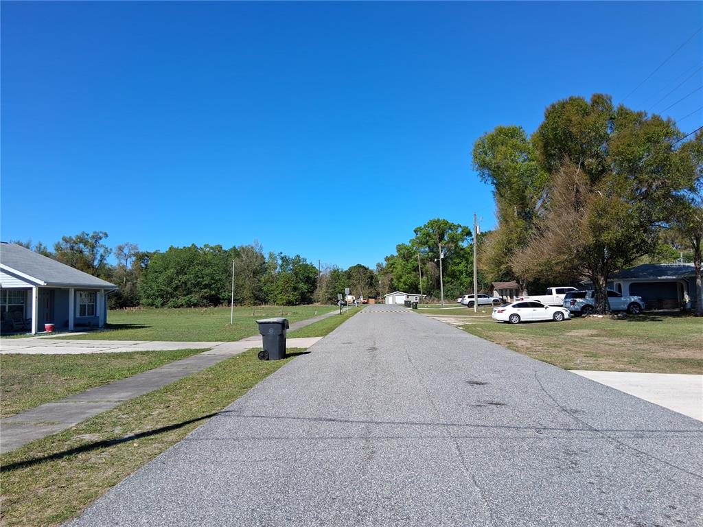 A white detached garage with a side carport and a concrete patio sits on grass — 515 BOITNOTT LANE, BUSHNELL, FL