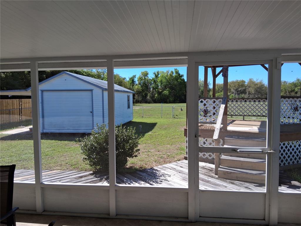 A wooden gazebo with lattice skirting stands in a grassy backyard next to a deck — 515 BOITNOTT LANE, BUSHNELL, FL