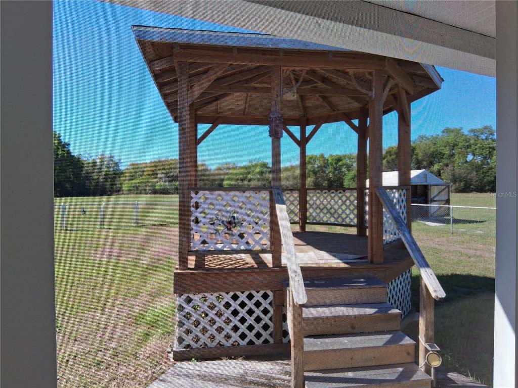 A wooden gazebo with lattice skirting and stairs sits in a grassy backyard — 515 BOITNOTT LANE, BUSHNELL, FL