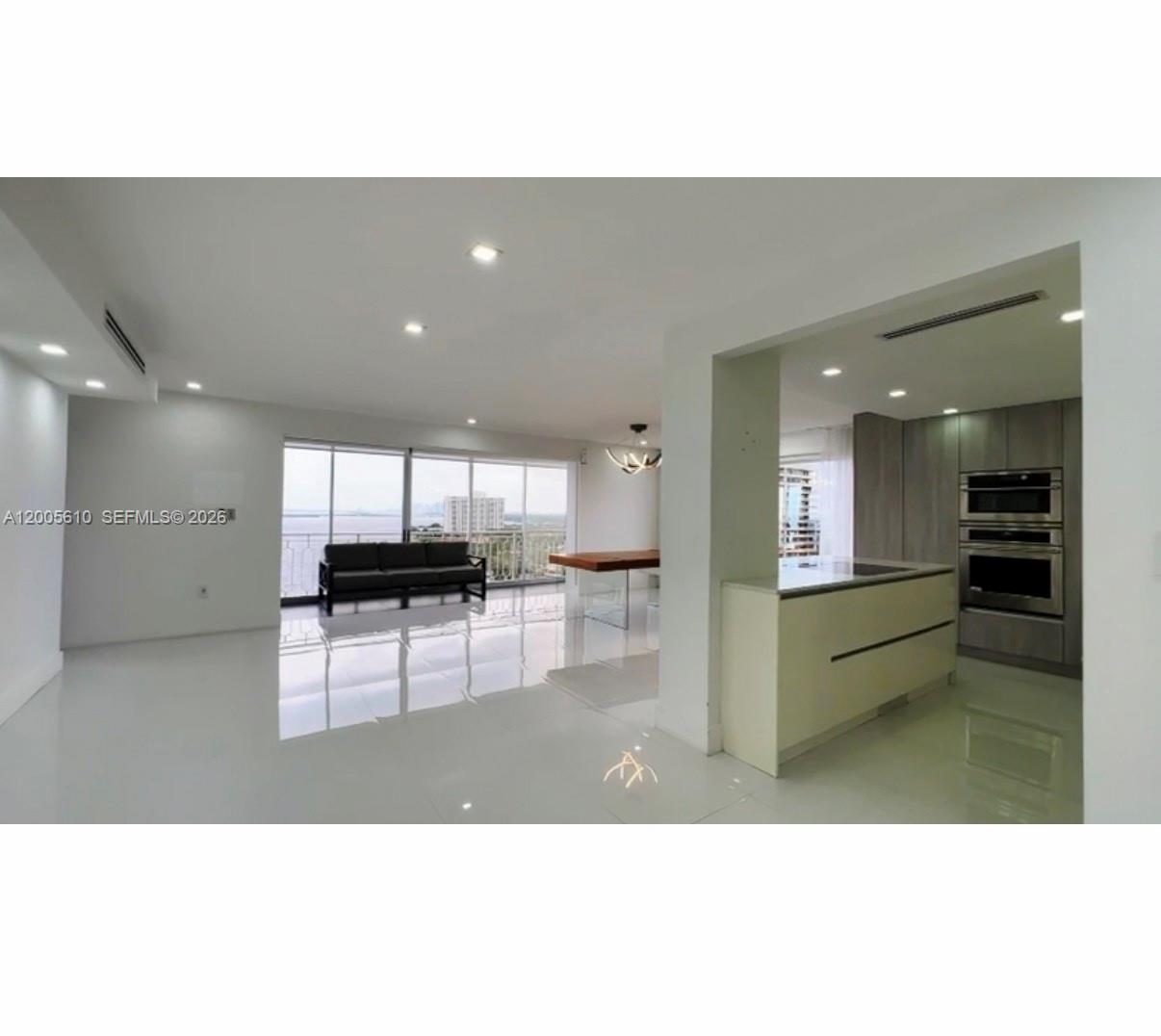 A modern open-concept living area features white tile floors, a kitchen island, and floor-to-ceiling windows — 11111 biscayne blvd # 1815, Miami FL 33181, MIAMI, FL