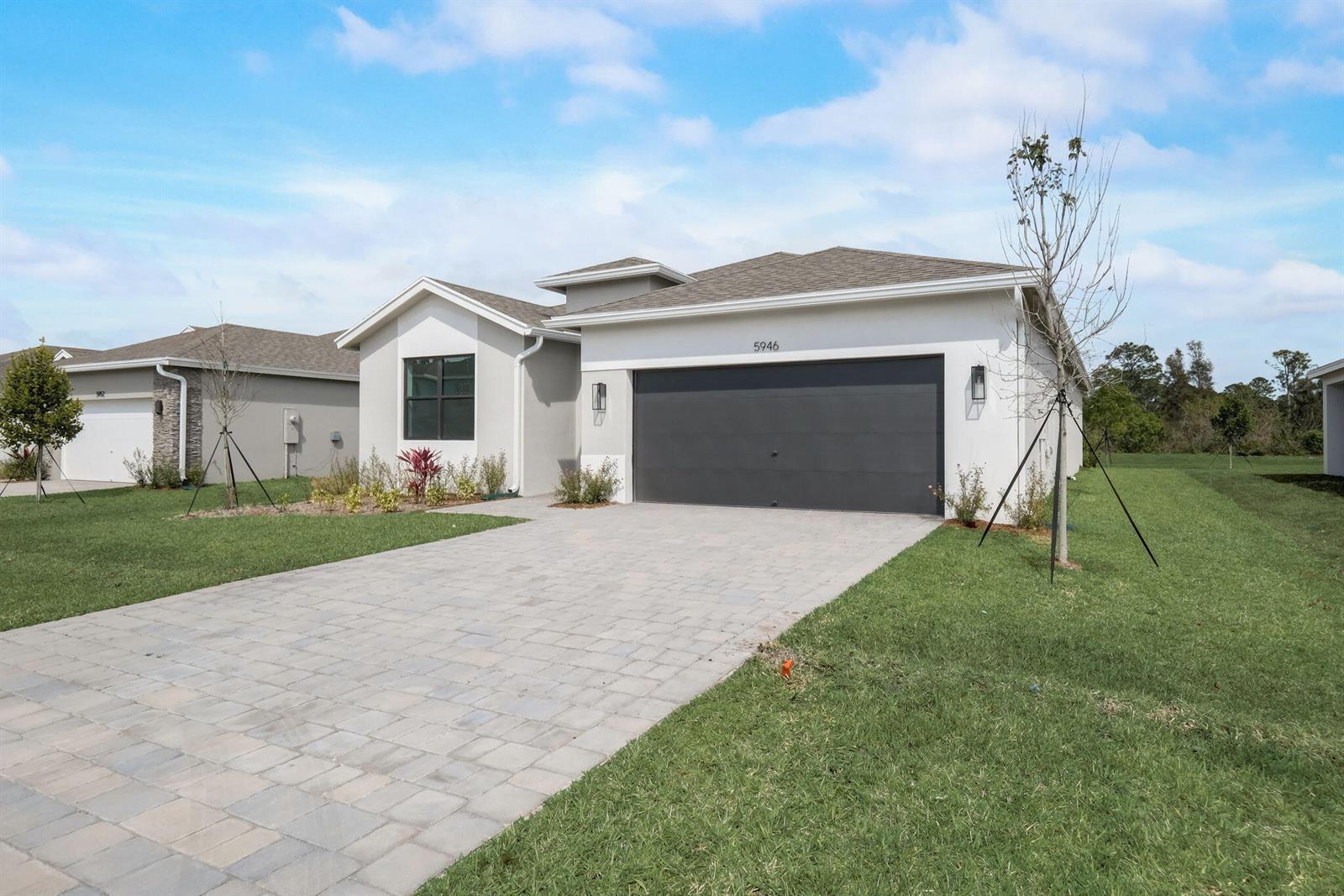 A modern one-story house with a gray garage door and a paved driveway — 5946 SE Skyblue Circle, Stuart FL 34997, STUART, FL