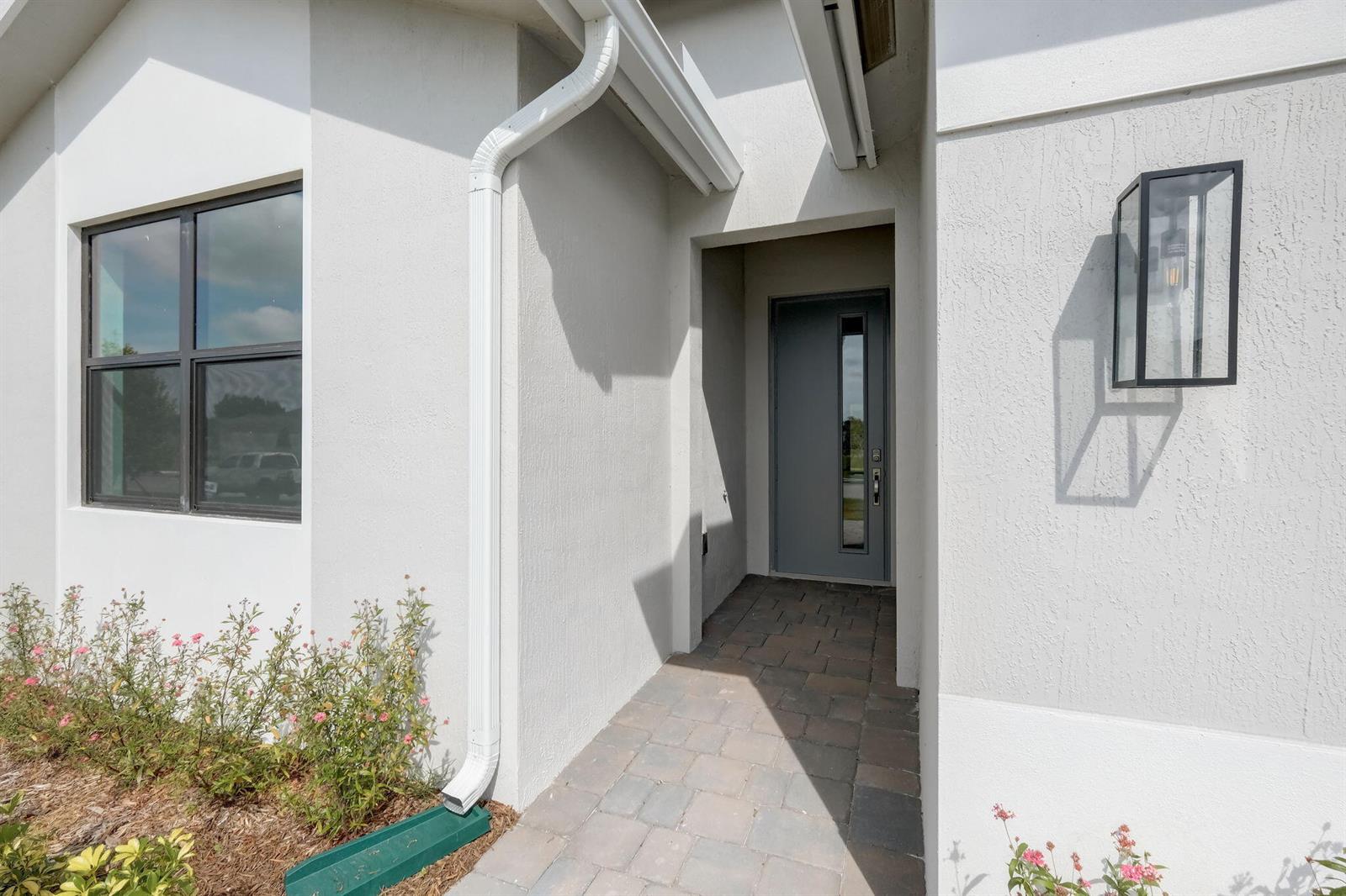 A modern home entrance features a gray door, a white downspout, and a wall lantern — 5946 SE Skyblue Circle, Stuart FL 34997, STUART, FL