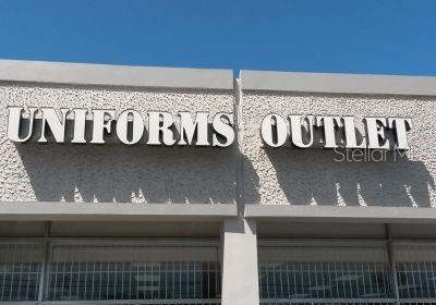 The exterior sign for a business named Uniforms Outlet is mounted on a textured wall — 90 ALONDRA ST., SAN JUAN, PR