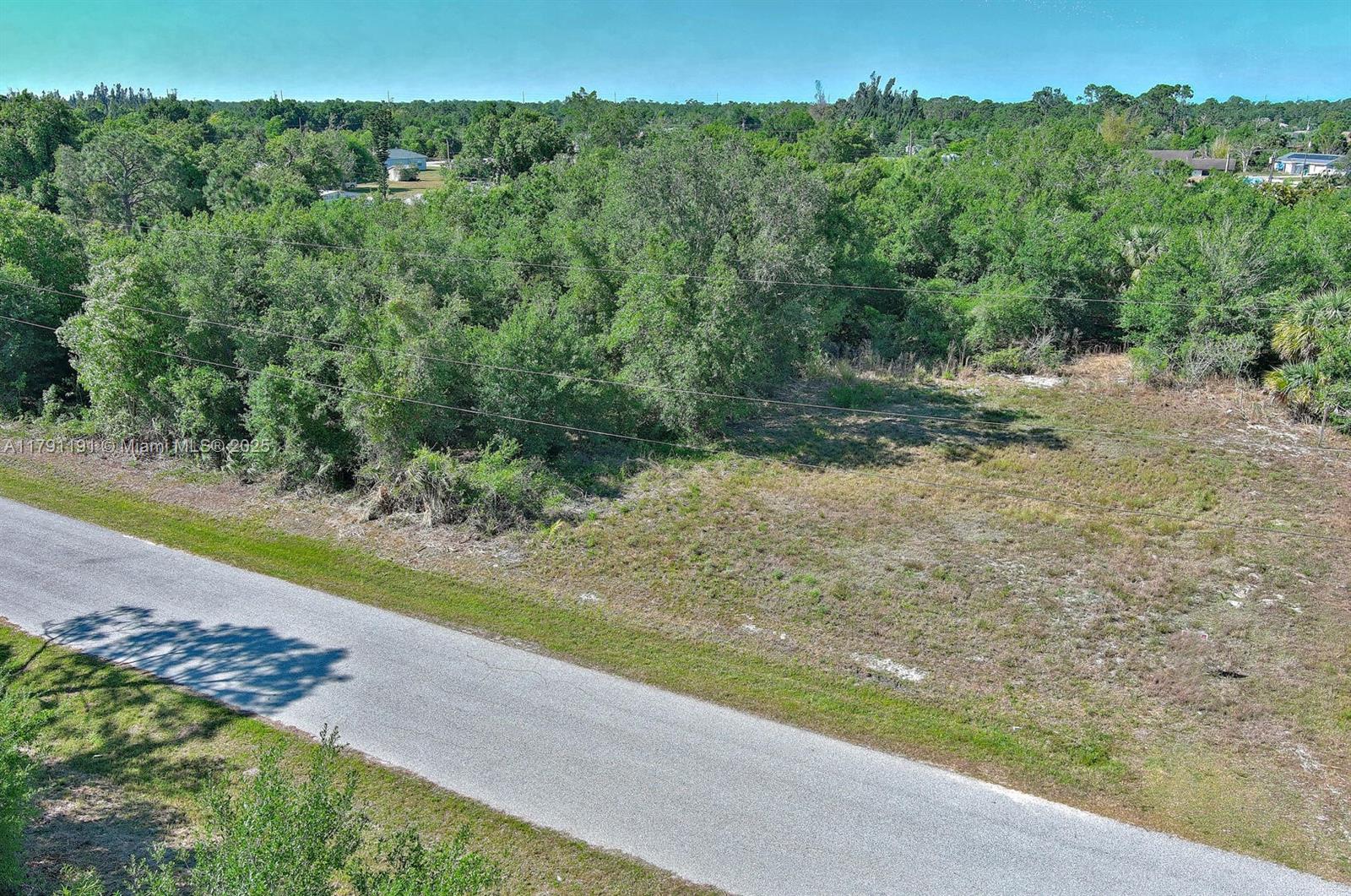 An elevated view shows a vacant, grassy lot bordered by a paved road and trees — 11117 1st Ave, Punta Gorda FL 33955, PUNTA GORDA, FL