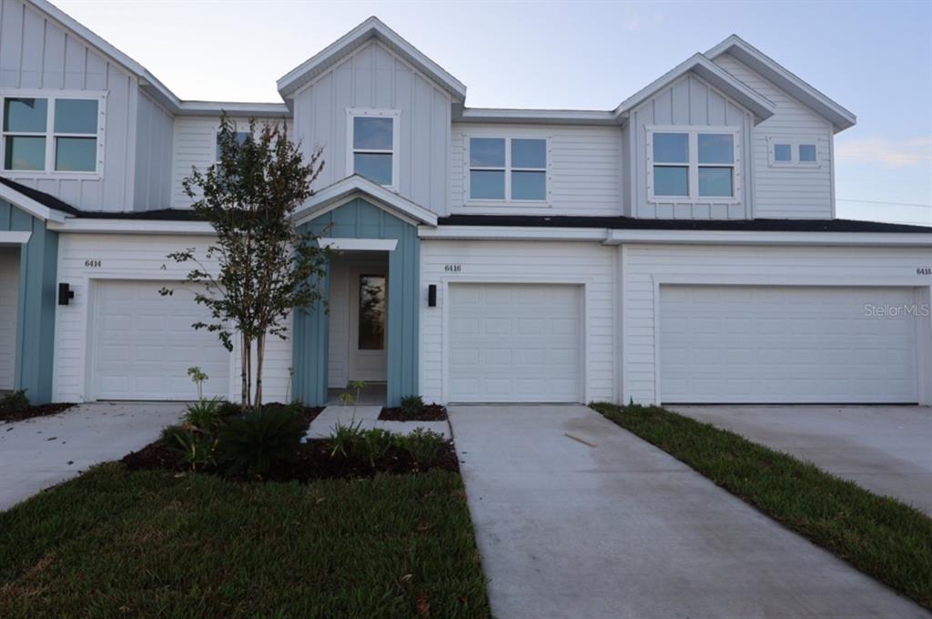 A row of three attached townhomes features white siding, blue accents, and individual garage doors — 6416 JENSEN VIEW AVENUE, APOLLO BEACH, FL