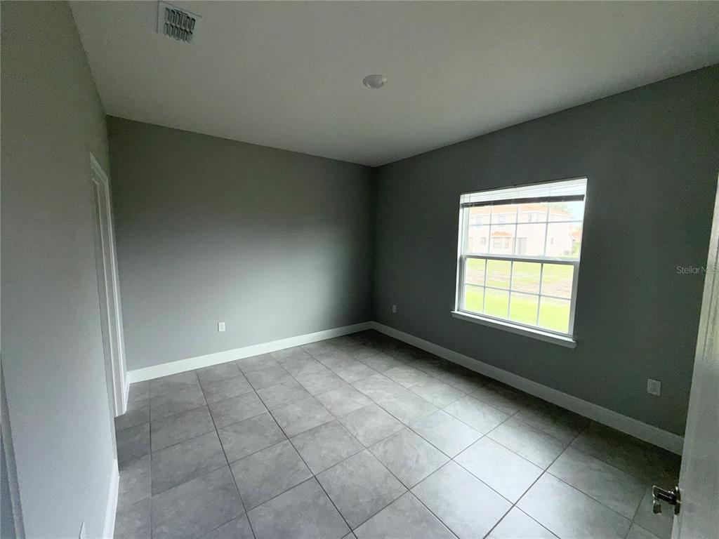 An empty room features gray walls, large square floor tiles, and a single window — 1808 CORIANDER DRIVE, KISSIMMEE, FL
