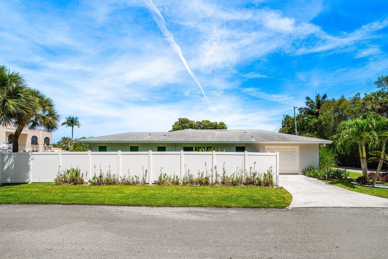A single-story house with a white vinyl fence, a concrete driveway, and palm trees — 106 Periwinkle Drive, Hypoluxo FL 33462, HYPOLUXO, FL