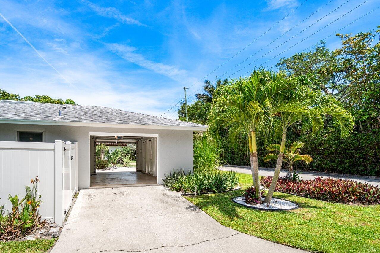 A concrete driveway leads to an open garage next to a palm tree and lawn — 106 Periwinkle Drive, Hypoluxo FL 33462, HYPOLUXO, FL