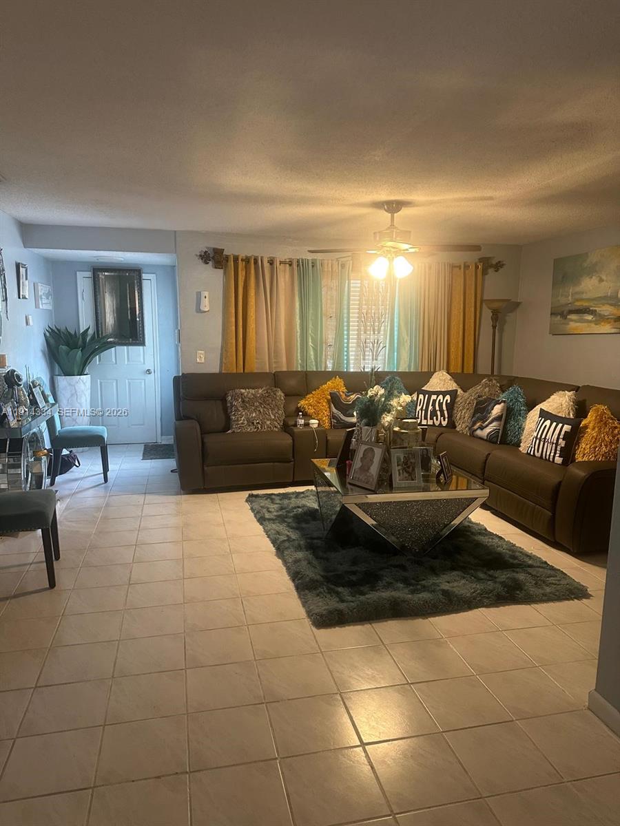 A living room features a large brown sectional sofa, a mirrored coffee table, and tile flooring — 9530 Sunset Strip, Sunrise FL 33322, SUNRISE, FL