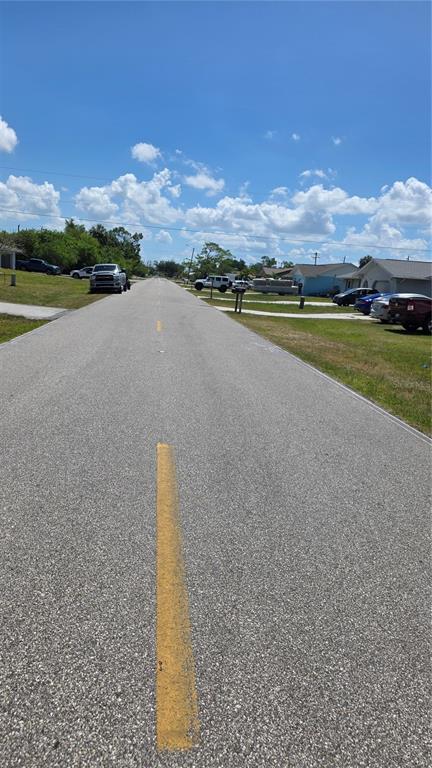 A paved residential street stretches into the distance under a bright, partly cloudy sky — 509 ORANGE DRIVE NW, PORT CHARLOTTE, FL