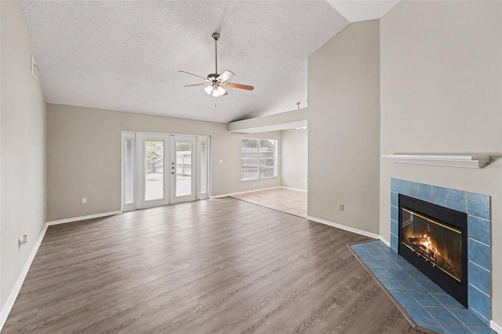A living room features wood-look flooring, a vaulted ceiling, and a blue-tiled fireplace — 8739 OSAGE DRIVE, TAMPA, FL