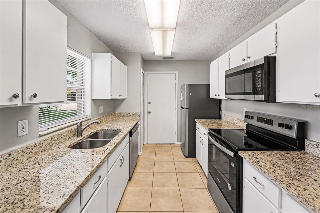 A galley kitchen features white cabinets, granite countertops, stainless steel appliances, and tile flooring — 8739 OSAGE DRIVE, TAMPA, FL