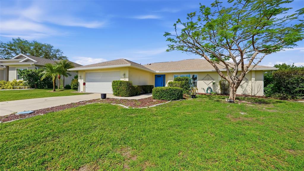 A single-story house with a light yellow exterior, a two-car garage, and a large tree — 26384 MADAGASCAR ROAD, PUNTA GORDA, FL