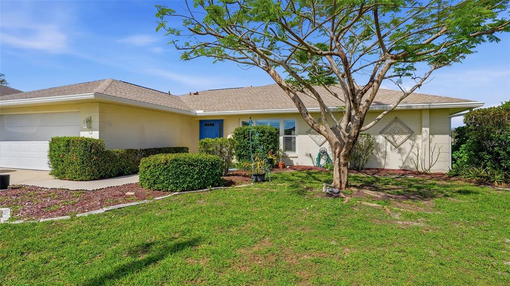 A single-story house with a light-colored exterior, a blue front door, and a large tree — 26384 MADAGASCAR ROAD, PUNTA GORDA, FL