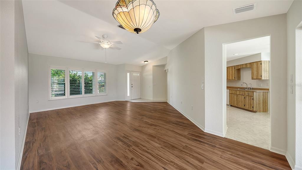 A living room with wood-look flooring, a ceiling fan, and a view into the kitchen — 26384 MADAGASCAR ROAD, PUNTA GORDA, FL