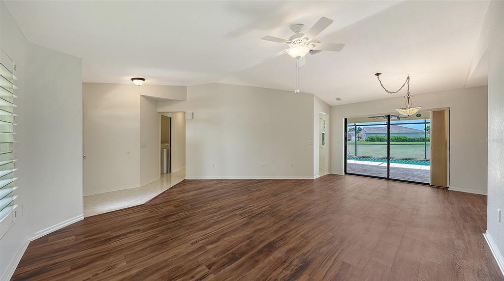 A spacious living room features dark wood-look flooring, white walls, a ceiling fan, and shutters — 26384 MADAGASCAR ROAD, PUNTA GORDA, FL