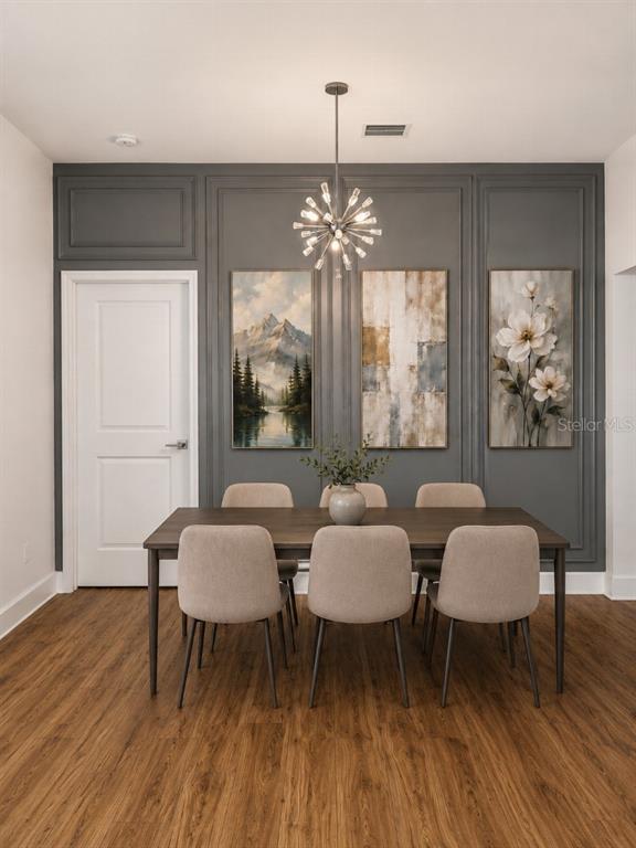 A dining room features a dark gray paneled wall, three framed artworks, and a modern chandelier — 108 MISSION HILLS AVENUE, TAMPA, FL