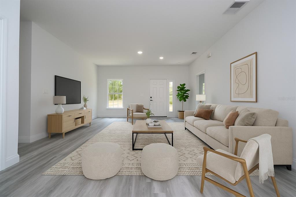 A bright living room features light wood furniture, a beige sofa, and grey wood-look flooring — 2580 GALLARDIA DRIVE, INDIAN LAKE ESTATES, FL