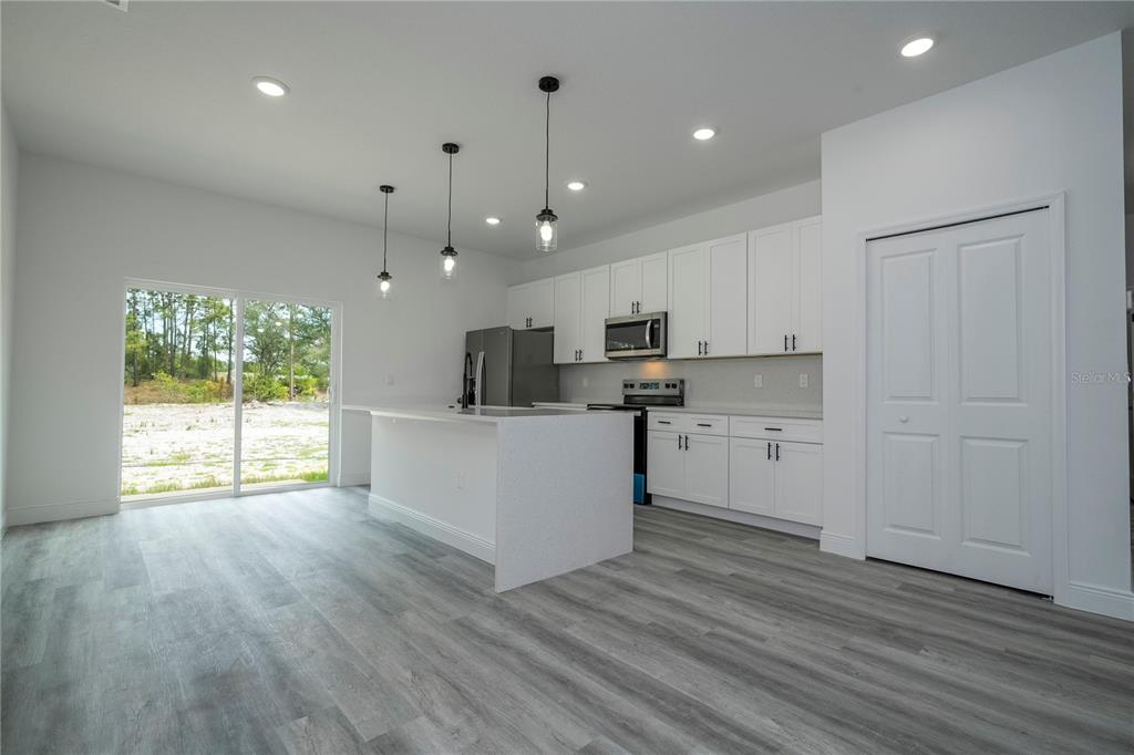 A modern kitchen features white cabinets, stainless steel appliances, a center island, and wood-look flooring — 2580 GALLARDIA DRIVE, INDIAN LAKE ESTATES, FL