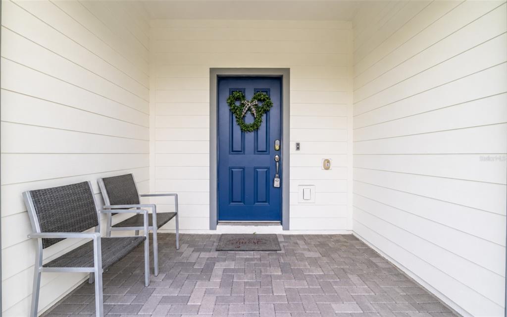 A covered front porch features a blue door with a wreath, two chairs, and pavers — 886 PARADISE DRIVE, DAVENPORT, FL