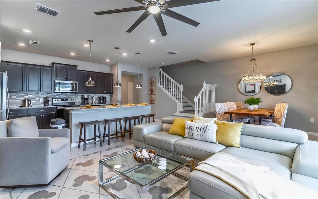 An open-concept kitchen and living area features dark cabinetry, a breakfast bar, and stairs — 886 PARADISE DRIVE, DAVENPORT, FL