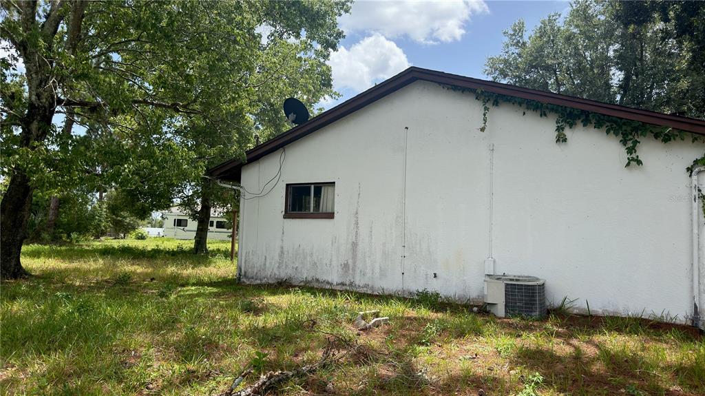 The exterior side of a white stucco house features a small window and an air conditioner — 621 ELDRON BOULEVARD SE, PALM BAY, FL