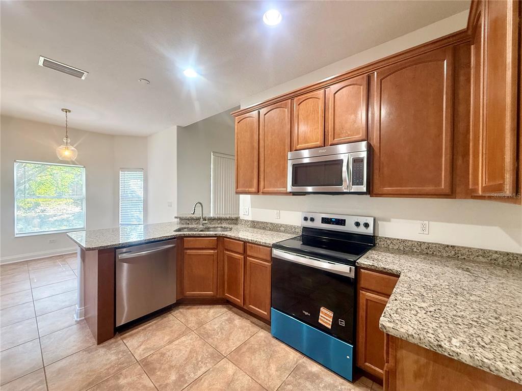 A kitchen features wood cabinets, granite countertops, stainless steel appliances, and tile flooring — 6984 BRESCIA WAY, ORLANDO, FL