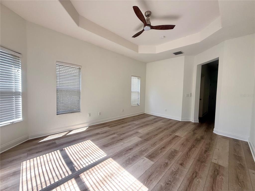An empty room features wood-look flooring, white walls, a tray ceiling, and a ceiling fan — 6984 BRESCIA WAY, ORLANDO, FL