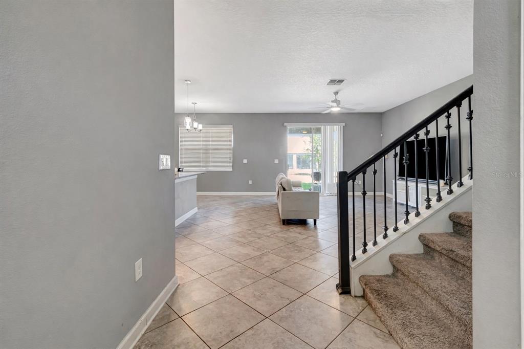 An open-concept living area features tile flooring, a staircase with black railings, and sliding glass doors — 4628 CORTLAND DRIVE, DAVENPORT, FL