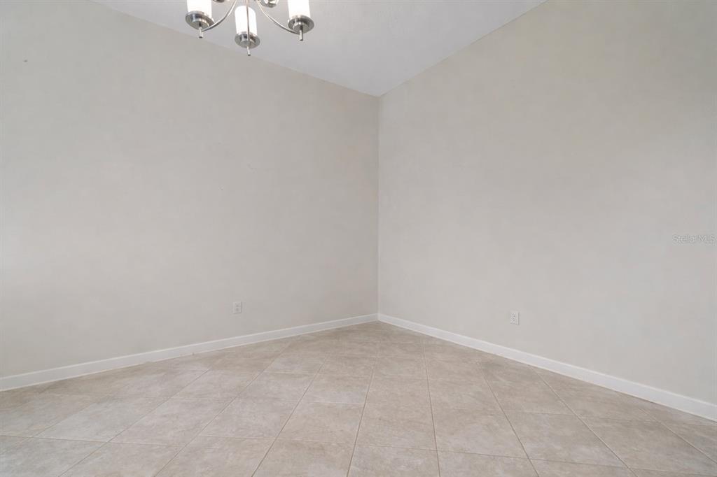 An empty room features beige tile flooring, light-colored walls, and a modern chandelier — 4628 CORTLAND DRIVE, DAVENPORT, FL