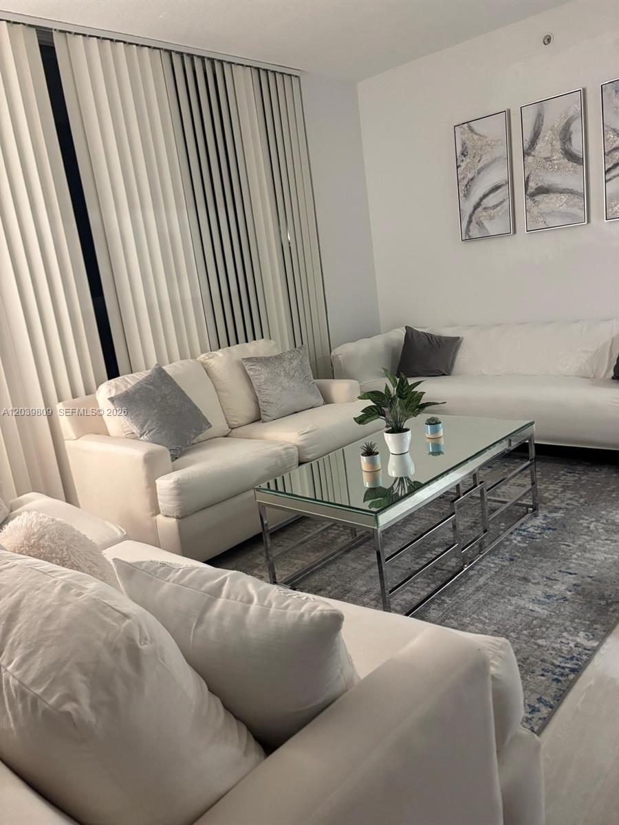 A living room features white sofas, a glass-topped coffee table, and abstract wall art — 601 NE 23rd St # 806, Miami FL 33137, MIAMI, FL