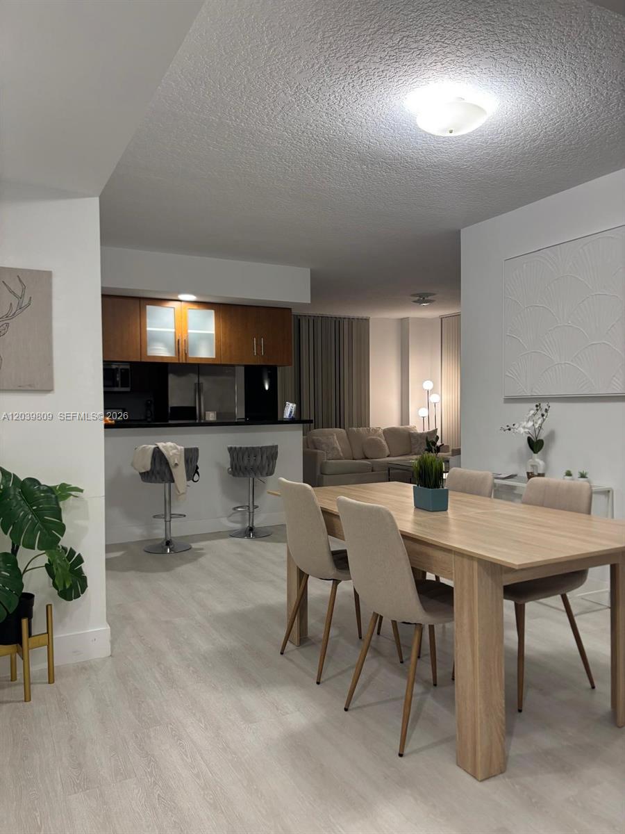 A dining area with a light wood table leads into a kitchen with bar seating — 601 NE 23rd St # 806, Miami FL 33137, MIAMI, FL