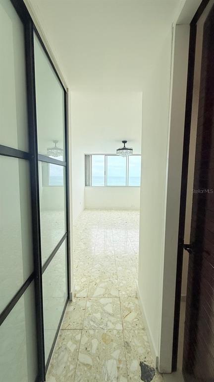 A hallway with light terrazzo flooring leads to a room with large windows overlooking the ocean — 0 ASHFORD AVE UNIT 1207, CONDADO, PR