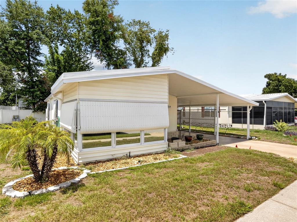 A single-story mobile home with a white exterior, a carport, and a small palm tree — 36419 BONNEY DRIVE, ZEPHYRHILLS, FL