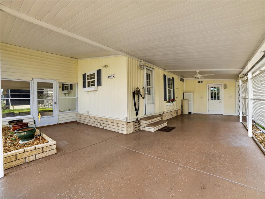 A covered carport with a concrete floor, brick planter, and two exterior doors — 36419 BONNEY DRIVE, ZEPHYRHILLS, FL