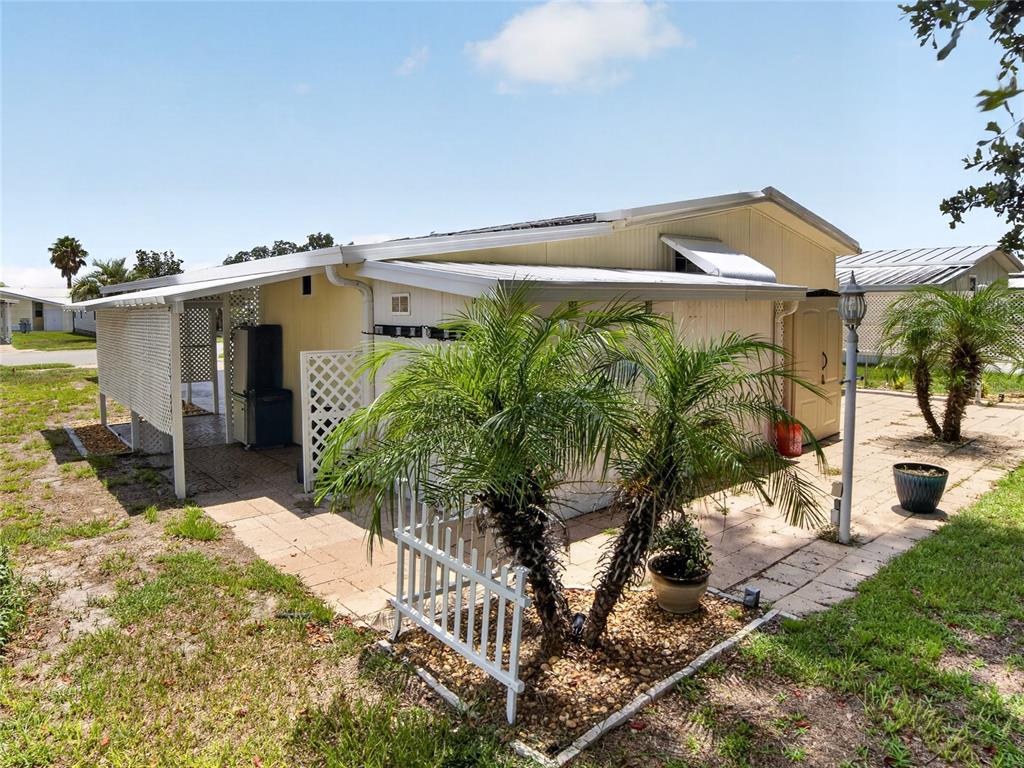 A mobile home exterior features a covered patio, a small white fence, and palm trees — 36419 BONNEY DRIVE, ZEPHYRHILLS, FL