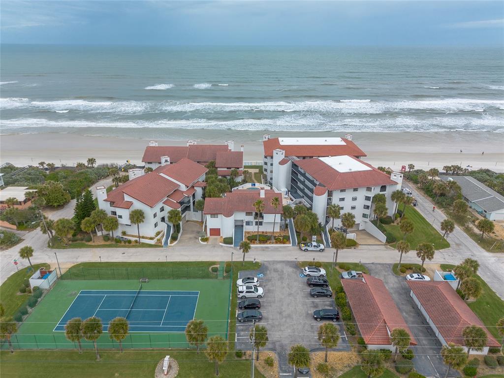 An aerial view shows a beachfront condominium complex with a tennis court and parking lot — 3001 S ATLANTIC AVENUE UNIT 300, NEW SMYRNA BEACH, FL