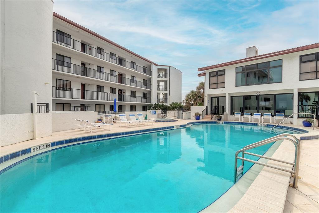 A swimming pool sits in a courtyard between a multi-story apartment building and a clubhouse — 3001 S ATLANTIC AVENUE UNIT 300, NEW SMYRNA BEACH, FL