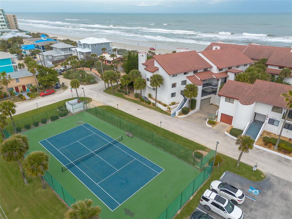 An aerial view shows a tennis court next to a multi-story building near the beach — 3001 S ATLANTIC AVENUE UNIT 300, NEW SMYRNA BEACH, FL