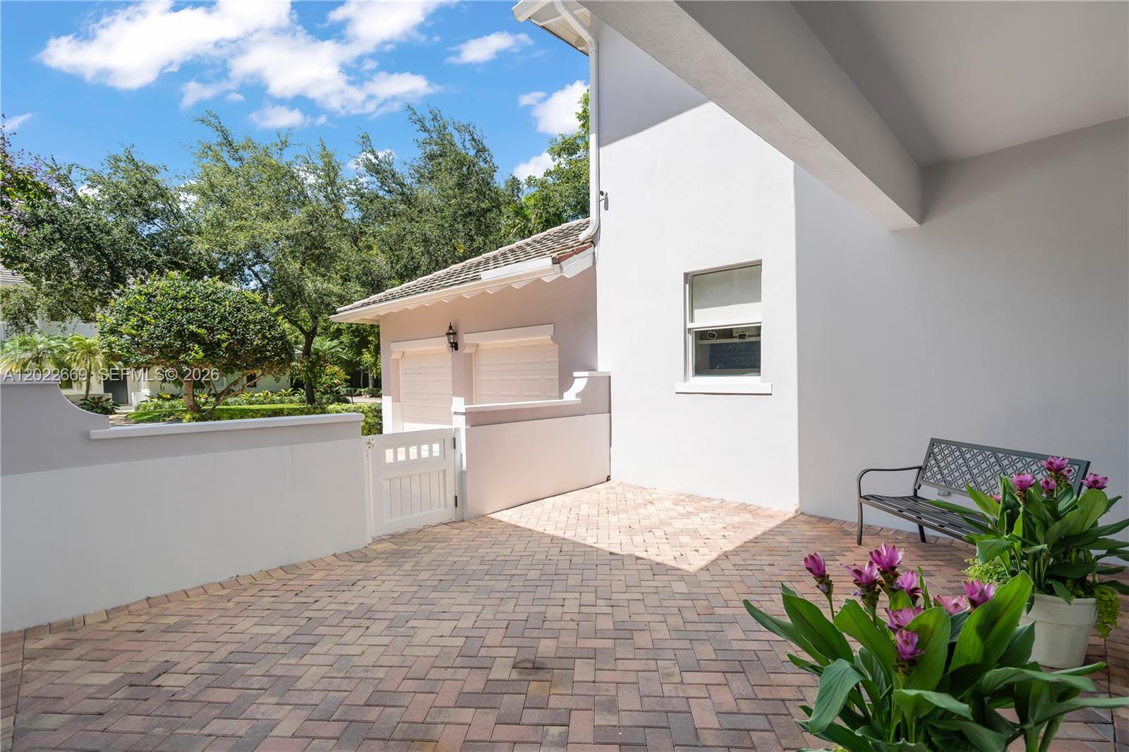 A paved patio features a metal bench, potted flowers, and a white gate — 5700 SW 86th St, South Miami FL 33143, SOUTH MIAMI, FL