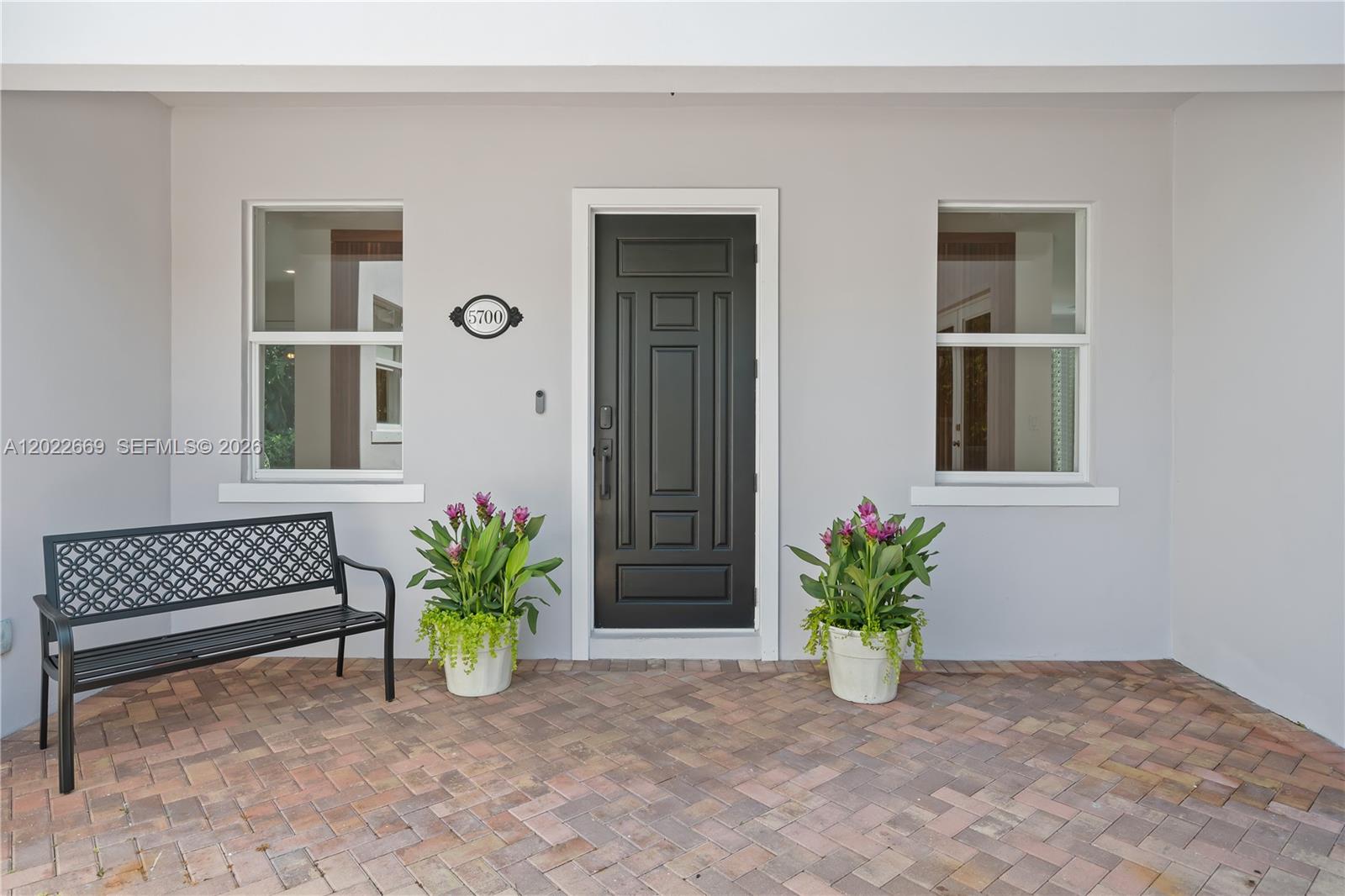 A front porch features a black door, two windows, a metal bench, and potted plants — 5700 SW 86th St, South Miami FL 33143, SOUTH MIAMI, FL