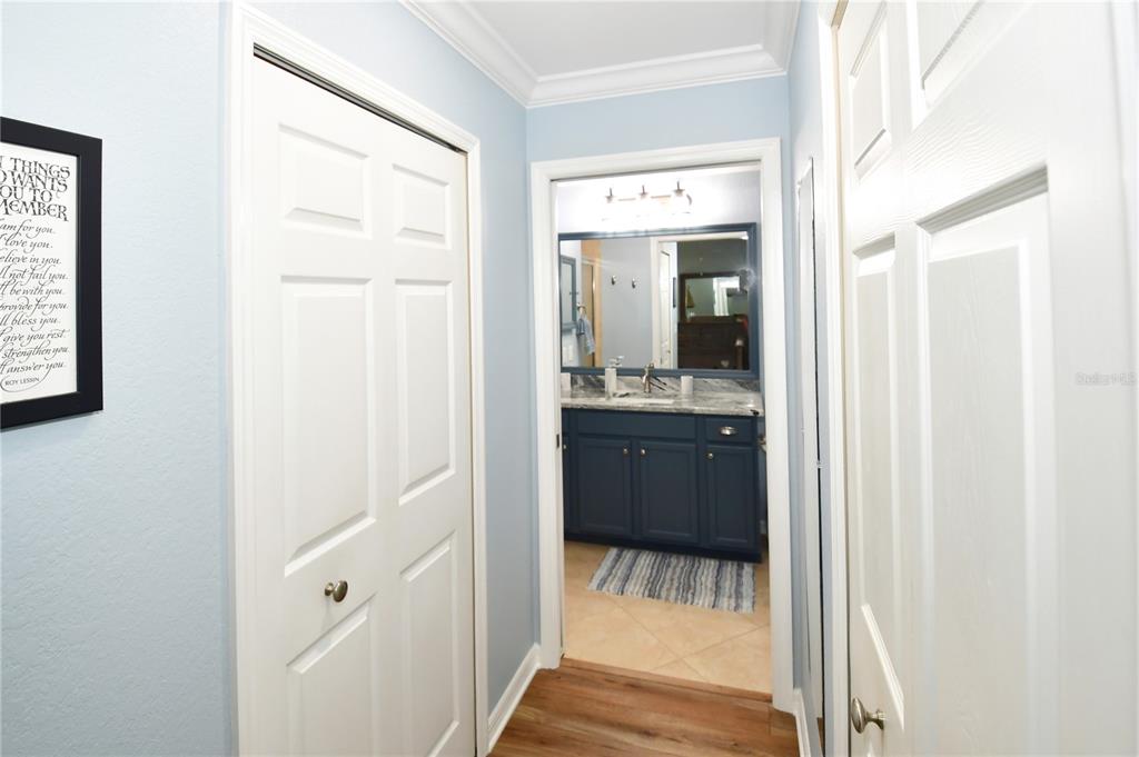 A hallway with white doors leads to a bathroom featuring a blue vanity and mirror — 7607 GRAND ESTUARY TRAIL UNIT 102, BRADENTON, FL