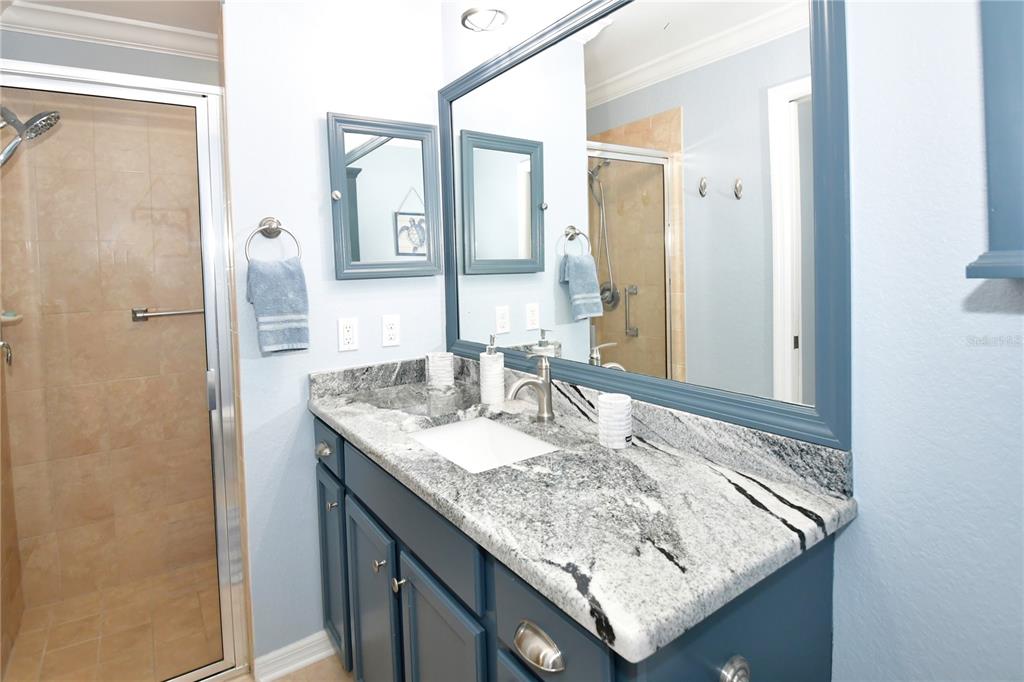 A bathroom features a blue vanity with a granite countertop, a mirror, and a shower — 7607 GRAND ESTUARY TRAIL UNIT 102, BRADENTON, FL