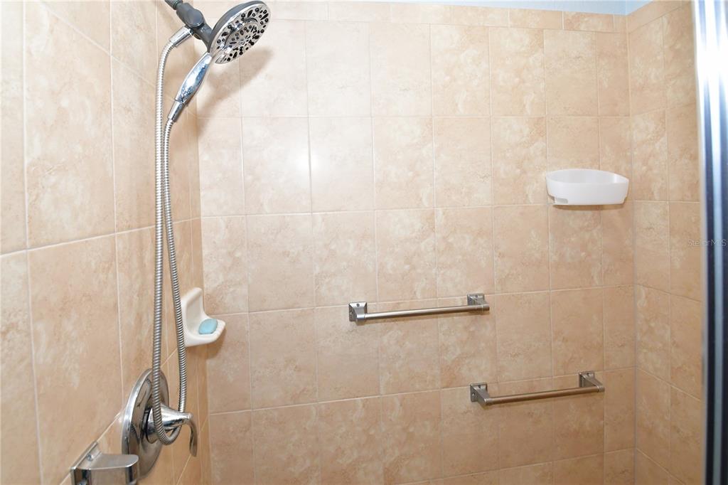 A tiled shower stall features a handheld showerhead, two grab bars, and a soap dish — 7607 GRAND ESTUARY TRAIL UNIT 102, BRADENTON, FL