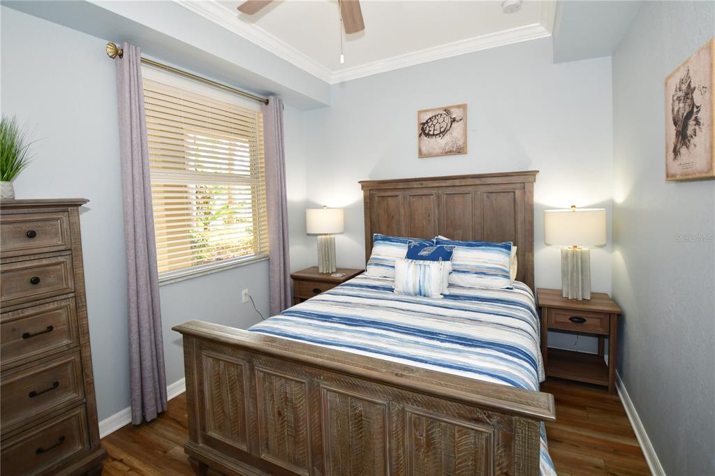 A bedroom features a wooden bed frame, two nightstands, a dresser, and blue-striped bedding — 7607 GRAND ESTUARY TRAIL UNIT 102, BRADENTON, FL