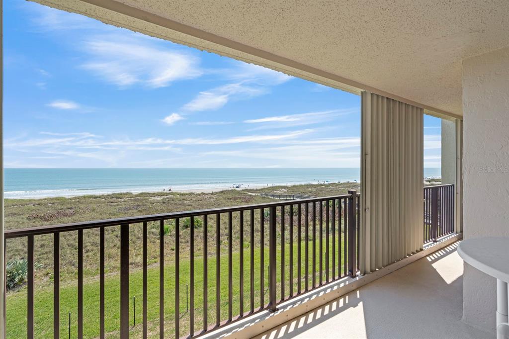 A balcony with a metal railing overlooks a grassy lawn, sand dunes, and the ocean — 1890 N ATLANTIC AVENUE UNIT A404, COCOA BEACH, FL