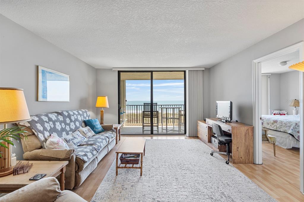 A living room features a sofa, desk, and sliding glass doors opening to a beach balcony — 1890 N ATLANTIC AVENUE UNIT A404, COCOA BEACH, FL